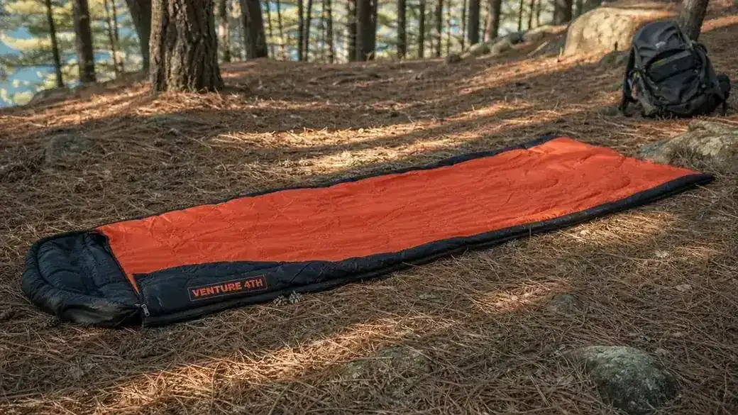 VENTURE 4TH mummy sleeping bag unrolled and laid out on pine needles at a campsite